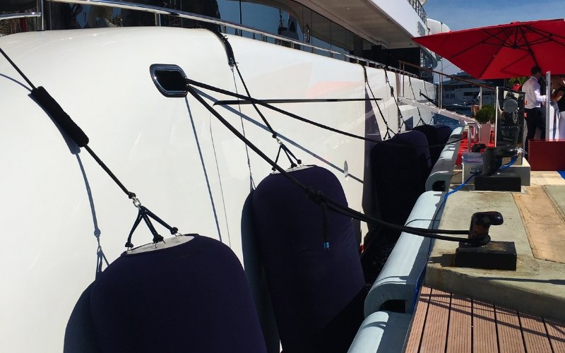 The side view of a sailing boat with black fenders resting against the marina platform, gently securing the boat in place