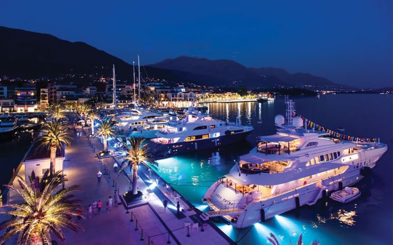 Luxury yachts docked at a marina in Montenegro at night, illuminated by stunning lights.