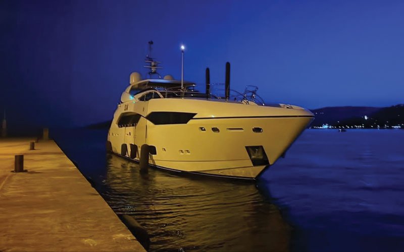 A luxurious mega yacht docked in a marina at night, with a dark blue sky and sea.