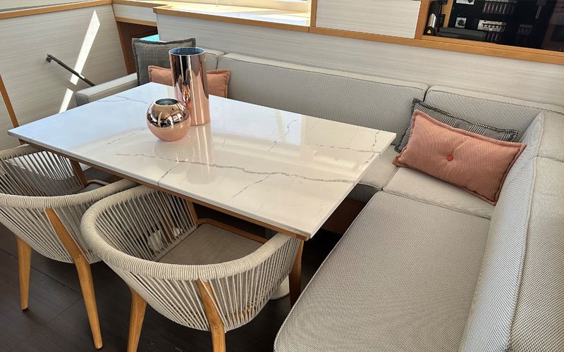 Exterior view of a yacht salon featuring upholstery designed by Argola Textile Yacht Design, with two decorative cushions in red and grey. In front, a table adorned with decorative metal objects, and two chairs placed in front