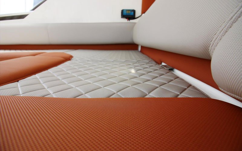 Close-up of a yacht seat in orange and white, featuring two textures, one of which is quilted