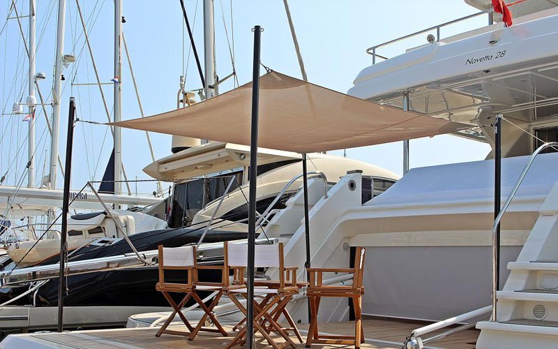 A white yacht anchored in a marina, with chairs at the front and a canopy from Argola Textile Yacht Design above