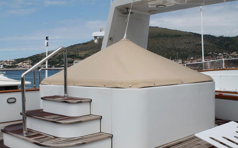 White yacht anchored in a marina, with three steps leading to a pool covered by a white Argola Textile Yacht Design cover. Sleek, modern design with a minimalist, luxurious feel