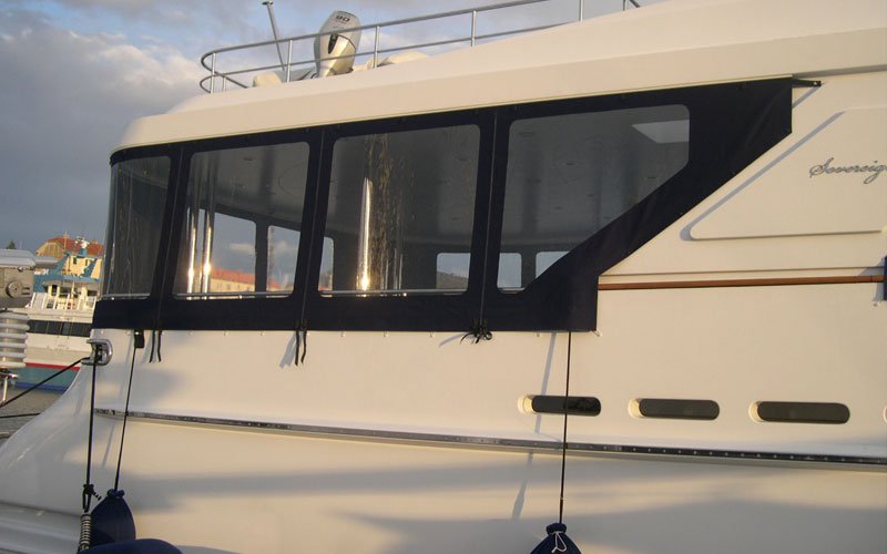 White yacht anchored in a marina, with black window covers designed by Argola Textile Yacht Design, creating a stylish and modern look