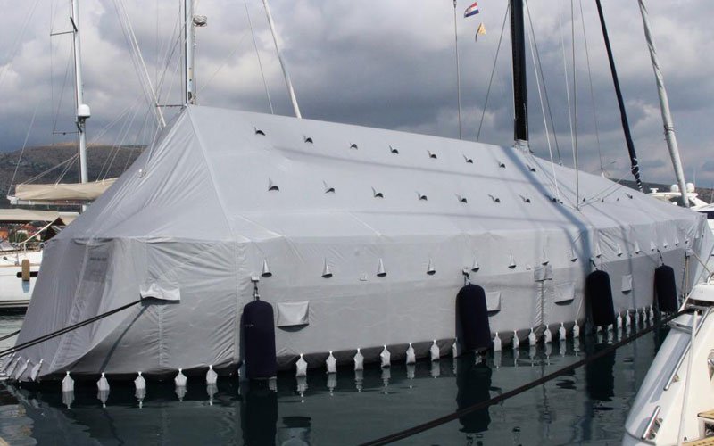 Sailing yacht anchored in a marina, completely covered with a white cover designed by Argola Textile Yacht Design, giving it a sleek, modern appearanc
