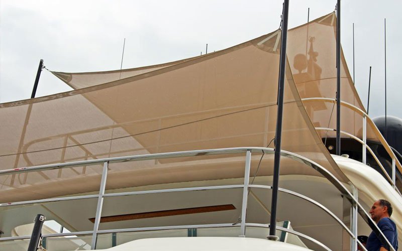 Sailing yacht anchored in a marina, with two beige canopies designed by Argola Textile Yacht Design on the exterior, creating a stylish and shaded outdoor space