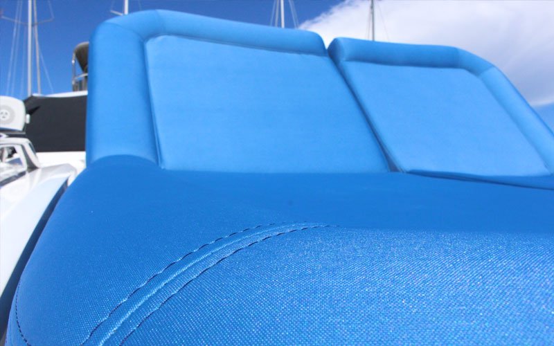 Detail of a blue furniture piece made from cushions on the upper exterior of a yacht anchored in a marina, designed by Argola Textile Yacht Design