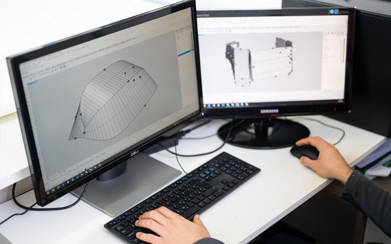 Hands of a person working on two computer screens, designing a yacht cover, with technical designs and blueprints visible on the screen