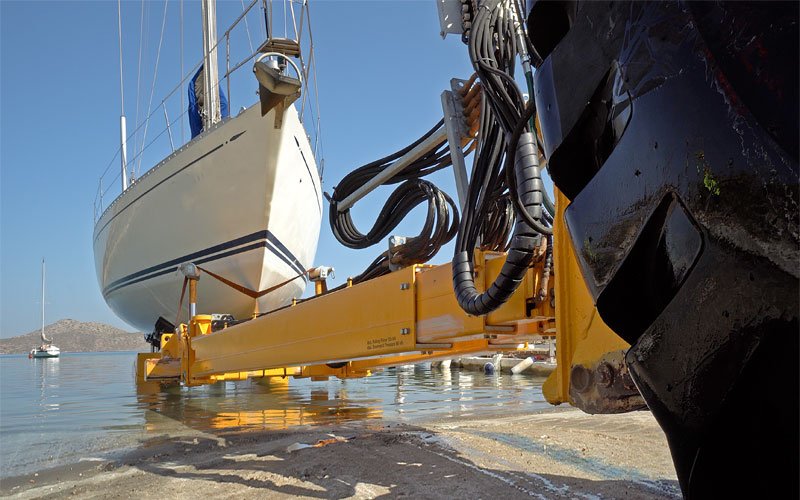 A yellow crane lifting a sailing yacht out of the water at Artemis Leros Boatyard, showcasing the boat hauling process