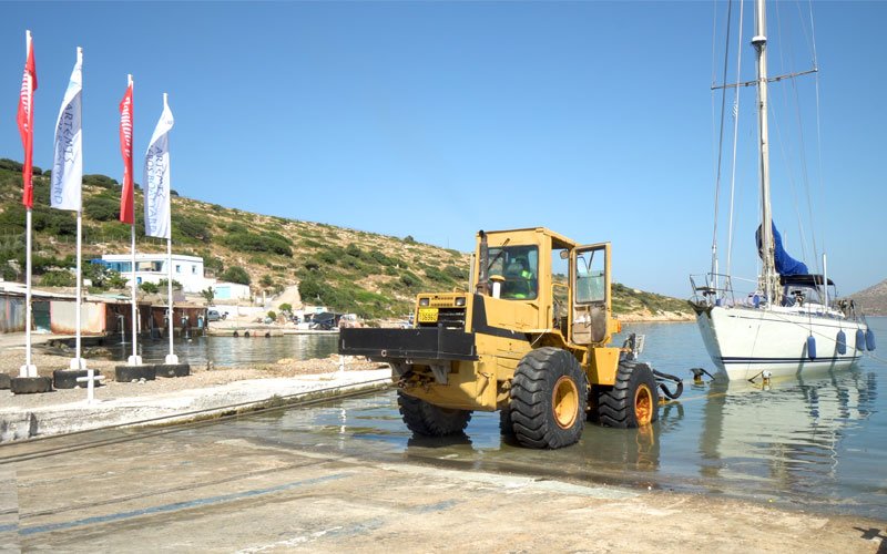 A yellow crane lifting a sailing yacht out of the water at Artemis Leros Boatyard, showcasing the boat hauling process