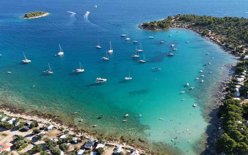 An idyllic bay near Betina with crystal-clear turquoise waters, small boats near the shore, and larger vessels further out