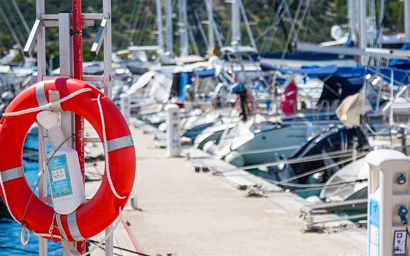 A row of sailing boats moored at the dock, neatly lined up against the calm waters, with a lifebuoy visible on the left