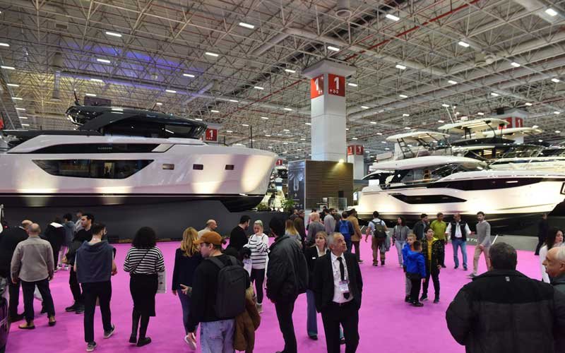 Visitors walk along a pink carpet between large yachts displayed indoors at the Bosphorus Boat Show | On Land.