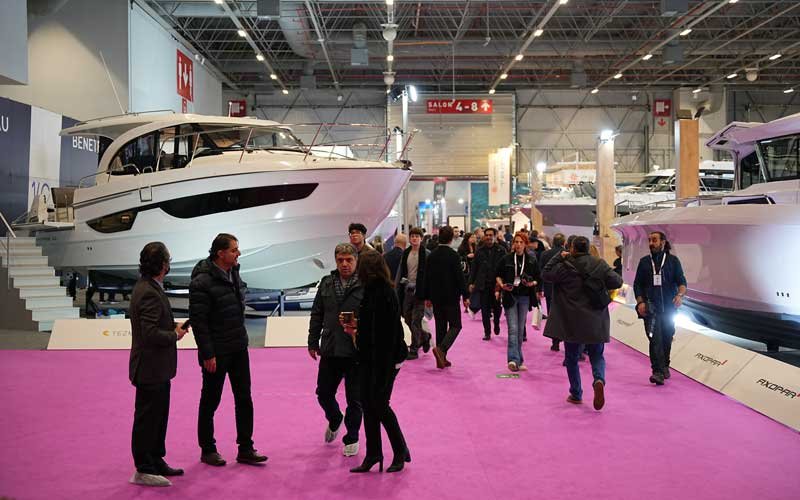 Visitors walk along a pink carpet between large yachts displayed indoors at the Bosphorus Boat Show | On Land
