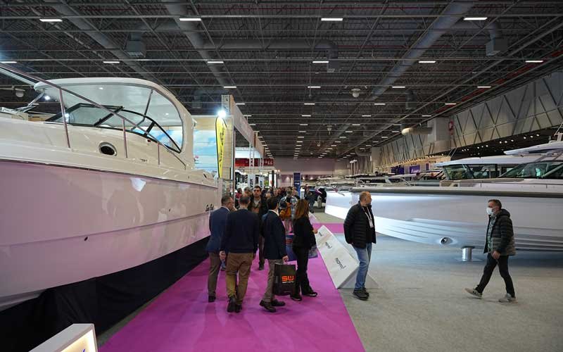 Visitors walk along a pink carpet between large yachts displayed indoors at the Bosphorus Boat Show | On Land