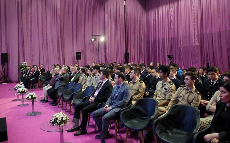 Attendees, including people in formal and military attire, are seated in a purple-draped hall at the Bosphorus Boat Show event.