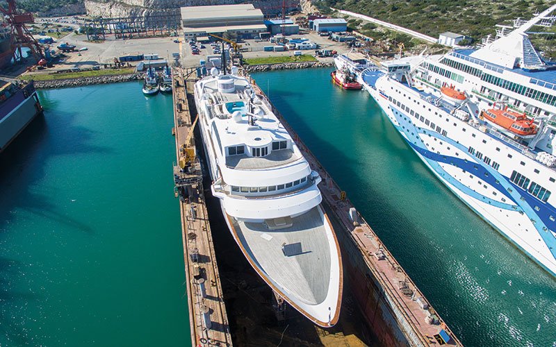 Close aerial view of Chalkis Shipyards with cruise ships, superyachts, and commercial vessels in dry dock and alongside the quay for repair, refit, and maintenance services.