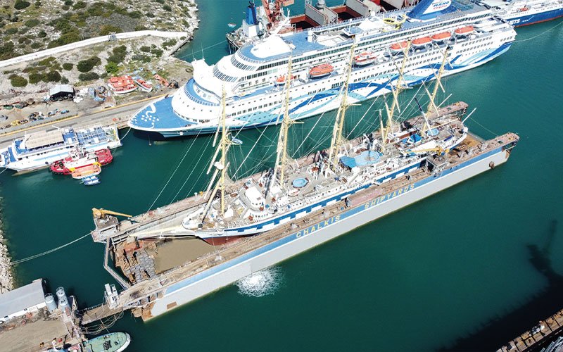 Close aerial view of Chalkis Shipyards with cruise ships, superyachts, and commercial vessels in dry dock and alongside the quay for repair, refit, and maintenance services.