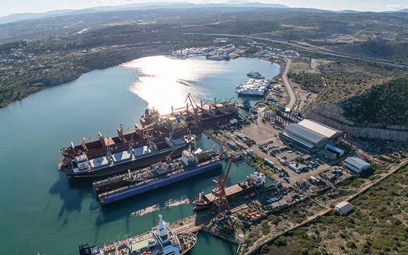 Aerial view of Chalkis Shipyards in Greece showing the ship repair and maintenance facilities, docks, and commercial vessels moored in the bay surrounded by coastal landscape.