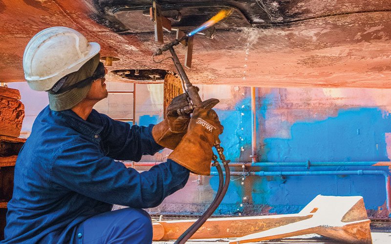 Skilled technicians working at Chalkis Shipyards performing welding, structural steel repairs, and propeller maintenance on vessels during ship repair and refit operations.