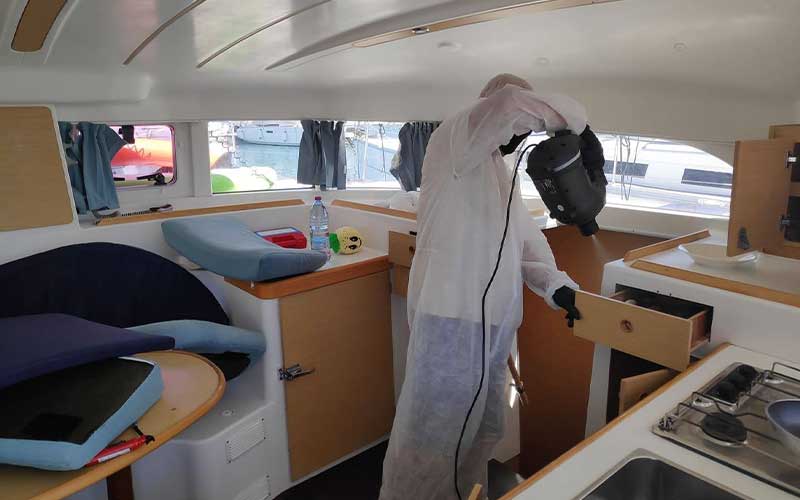 Crystal Clean technician in full protective suit disinfecting yacht deck with professional marine sprayer under clear blue sky