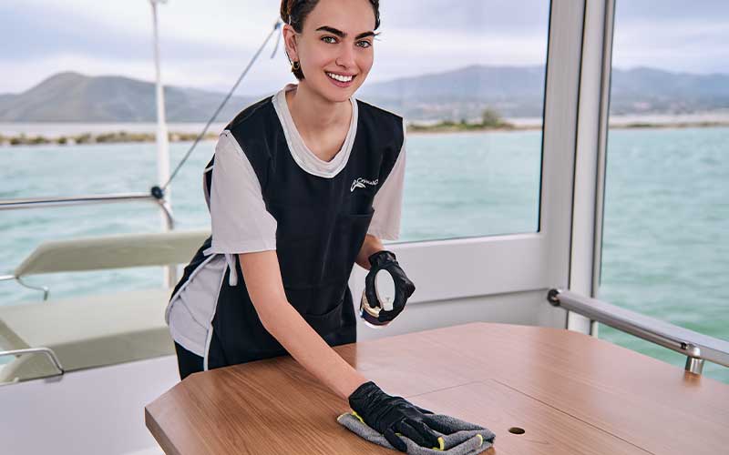 Crystal Clean staff wiping yacht table surface with eco‑friendly cleaning products near the sea.