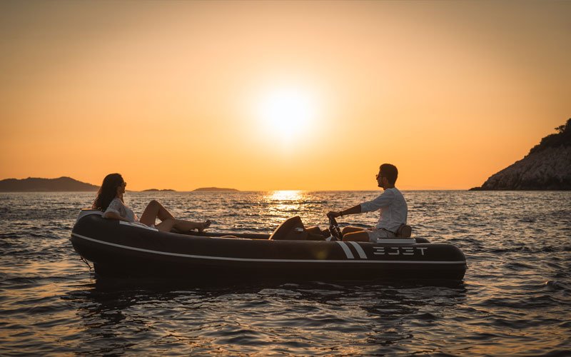 Ejet electric tender boat with three people relaxing on board during sunset, cruising on calm sea waters with scenic islands in the background