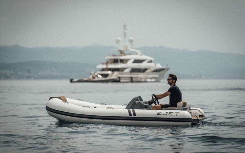 Man driving a jet-powered inflatable boat on the water, with a mega yacht at background