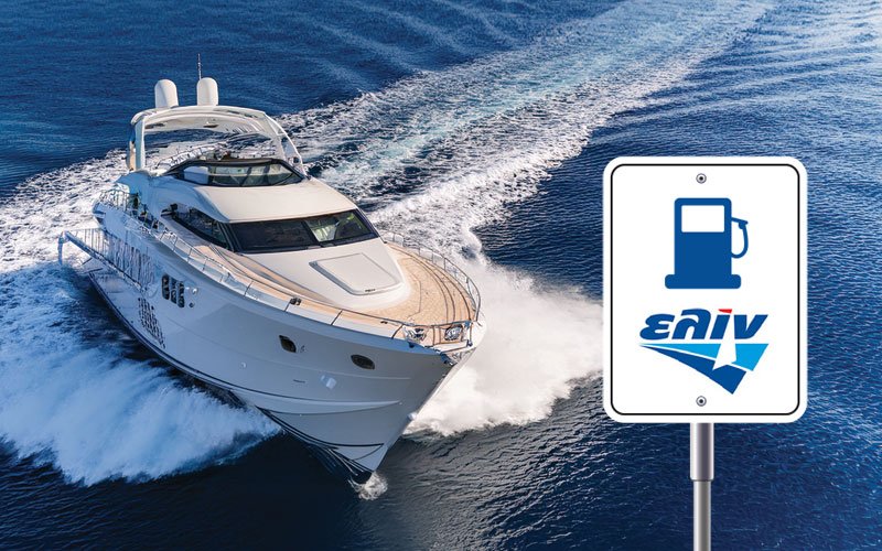A luxury white yacht cruising at high speed on the open sea, creating a wake behind it. In the foreground, a marine fuel station sign features a blue fuel pump icon and the logo of 'ΕΛΙΝ' (ELIN), a Greek fuel company