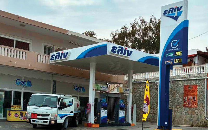 A fuel station branded with 'ΕΛΙΝ' (ELIN), a Greek petroleum company. The station includes a canopy over the pumps, a price sign showing fuel rates, and a white ELIN fuel truck parked nearby.