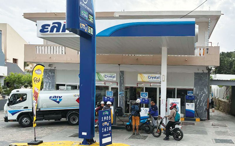 A fuel station branded with 'ΕΛΙΝ' (ELIN), a Greek petroleum company. The station includes a canopy over the pumps, a price sign showing fuel rates, and a white ELIN fuel truck parked nearby.