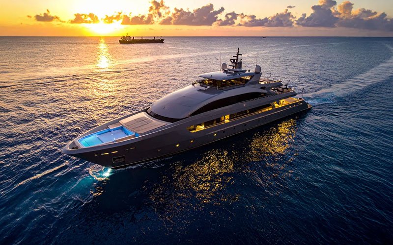 Aerial drone view of a luxury yacht sailing across deep blue ocean waters at sunset.