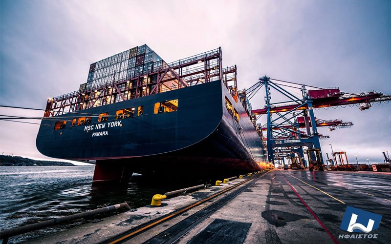 Cargo ship anchored at industrial port with cranes and maritime logistics infrastructure.