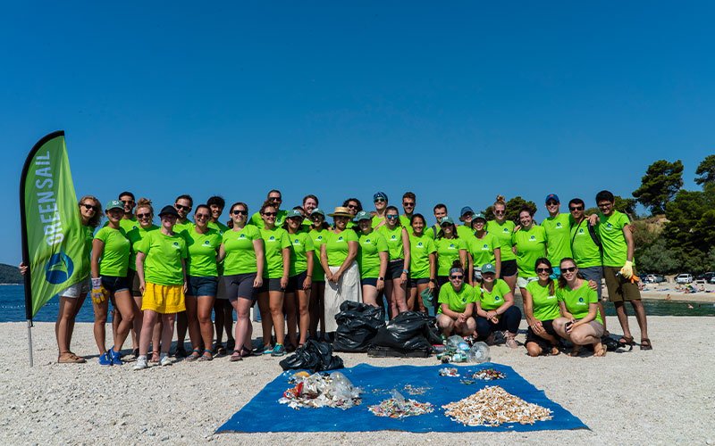 A team of people wearing green t-shirts with the logo of Green Sail they have been picking up trash from the beach