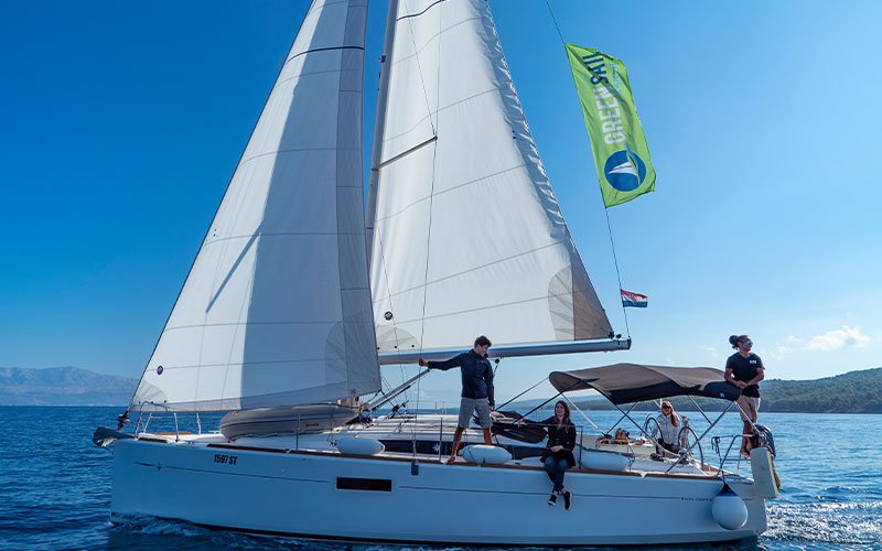 four people on a sailing yacht and a green flag og Green Sail.