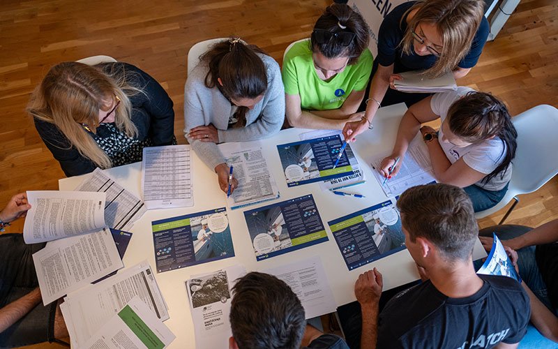 A team of people, around a table, worling together, having leaflets of Green Sail
