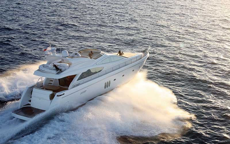 Luxury motor yacht cruising at high speed over open sea waters during sunset, creating dynamic water spray, with passengers relaxing on the deck.