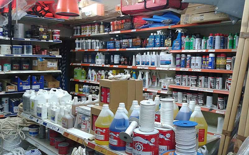 Interior of the LIANOS NIKOLAOS store showcasing a wide range of marine supplies, including ropes, paints, cleaning products, lubricants, flags, boat steering wheels, and various marine accessories neatly organized on shelves.