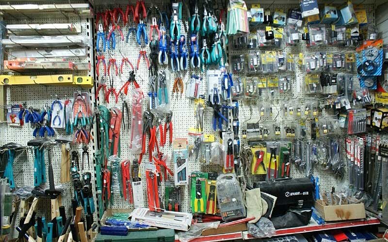 Wall display inside the LIANOS NIKOLAOS store featuring a wide selection of hand tools, including pliers, hammers, cutters, levels, and various accessories, all neatly arranged on pegboards and shelves.