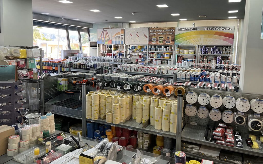An interior view of "Marinakis Xroma" showing neatly arranged shelves stocked with a variety of paint products and tools.