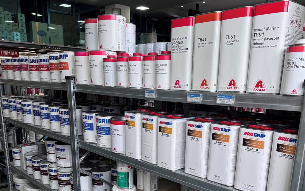 An interior view of "Marinakis Xroma" showing neatly arranged shelves stocked with a variety of paint products and tools.