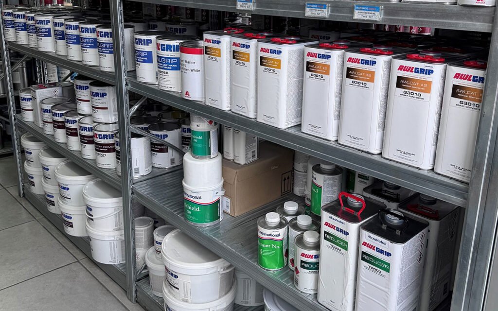 An interior view of "Marinakis Xroma" showing neatly arranged shelves stocked with a variety of paint products and tools.