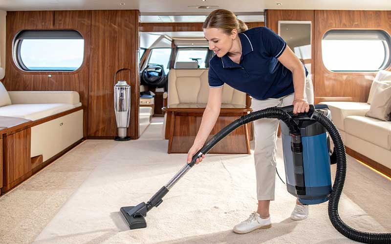 Cleaner vacuuming the carpet inside a spacious yacht living area using professional equipment.