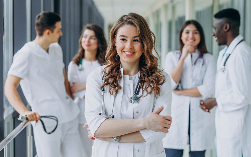 young female doctor standing in front of group of doctors in hospital corridor