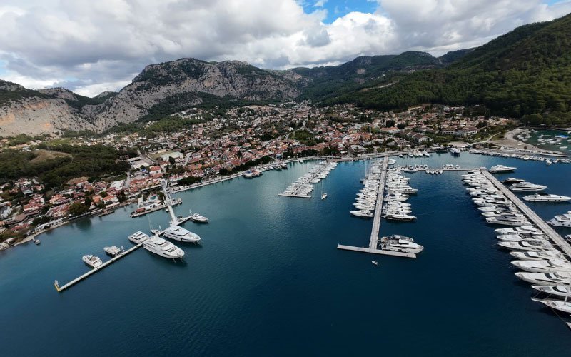 Small and large yachts docked in the marina, with houses and trees visible in the background