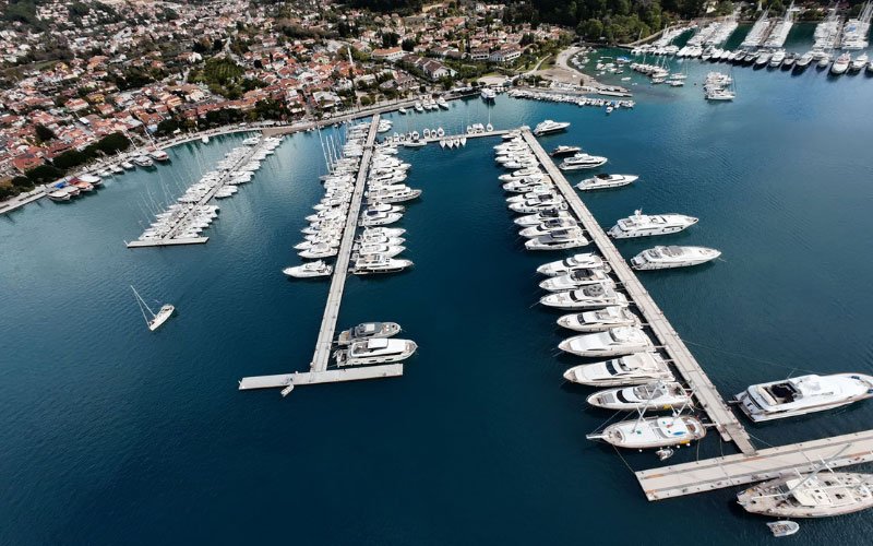 Small and large yachts docked in the marina, with houses and trees visible in the background