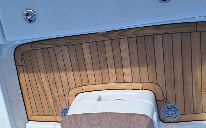 up of a yacht's teak deck, featuring a raised, curved step with a symmetrical plank pattern. The deck has a warm, natural wood tone with visible grain and black caulking lines.