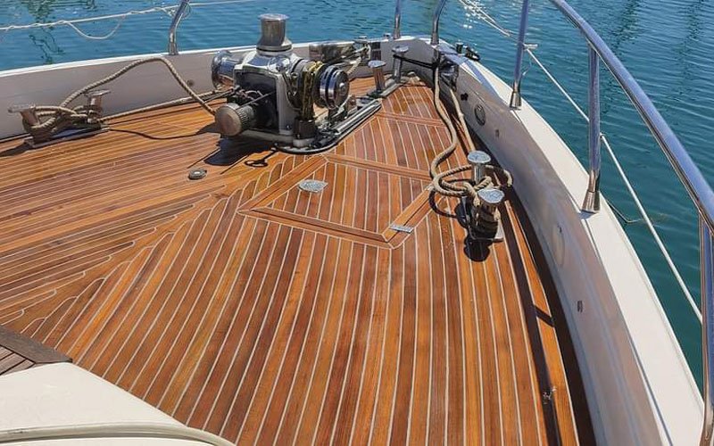 up of a yacht's teak deck, featuring a raised, curved step with a symmetrical plank pattern. The deck has a warm, natural wood tone with visible grain and black caulking lines.