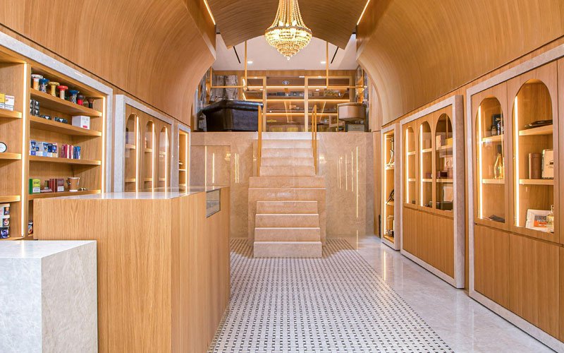Interior view of a modern cigar shop featuring a curved wooden ceiling, elegant chandeliers, display cabinets with cigars, and warm ambient lighting