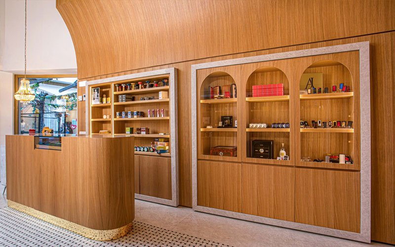 interior of a modern luxury cigar shop with wooden cabinetry, a curved wooden ceiling, and glass display shelves featuring cigars, lighters, and accessories. A chandelier hangs above the wooden counter